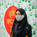 Portrait of a young woman wearing a hijab and mask against a colorful backdrop in Bangladesh.