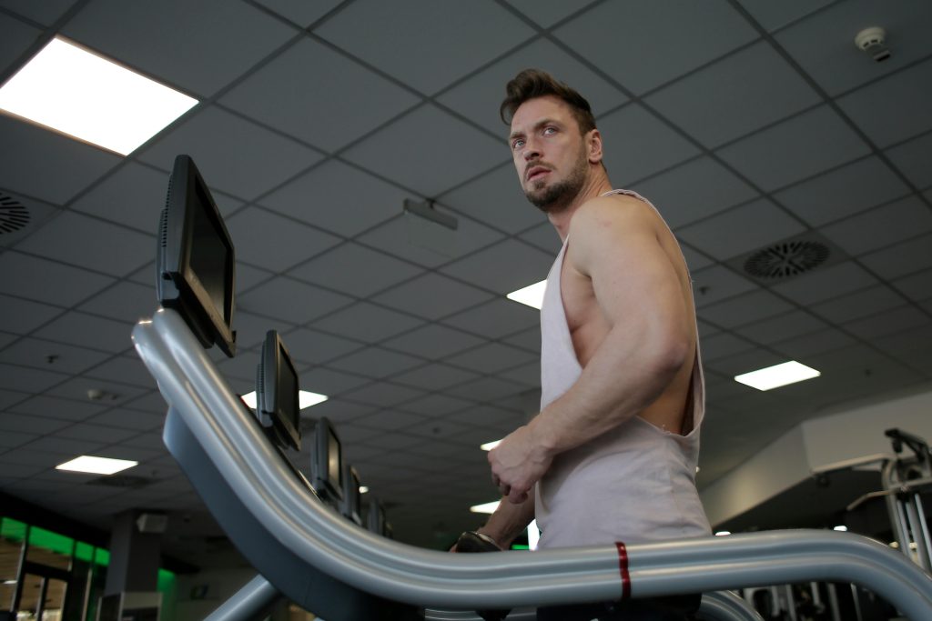 Low angle of muscular adult male athlete in sportswear during training on running machine in modern spacious fitness center while looking away